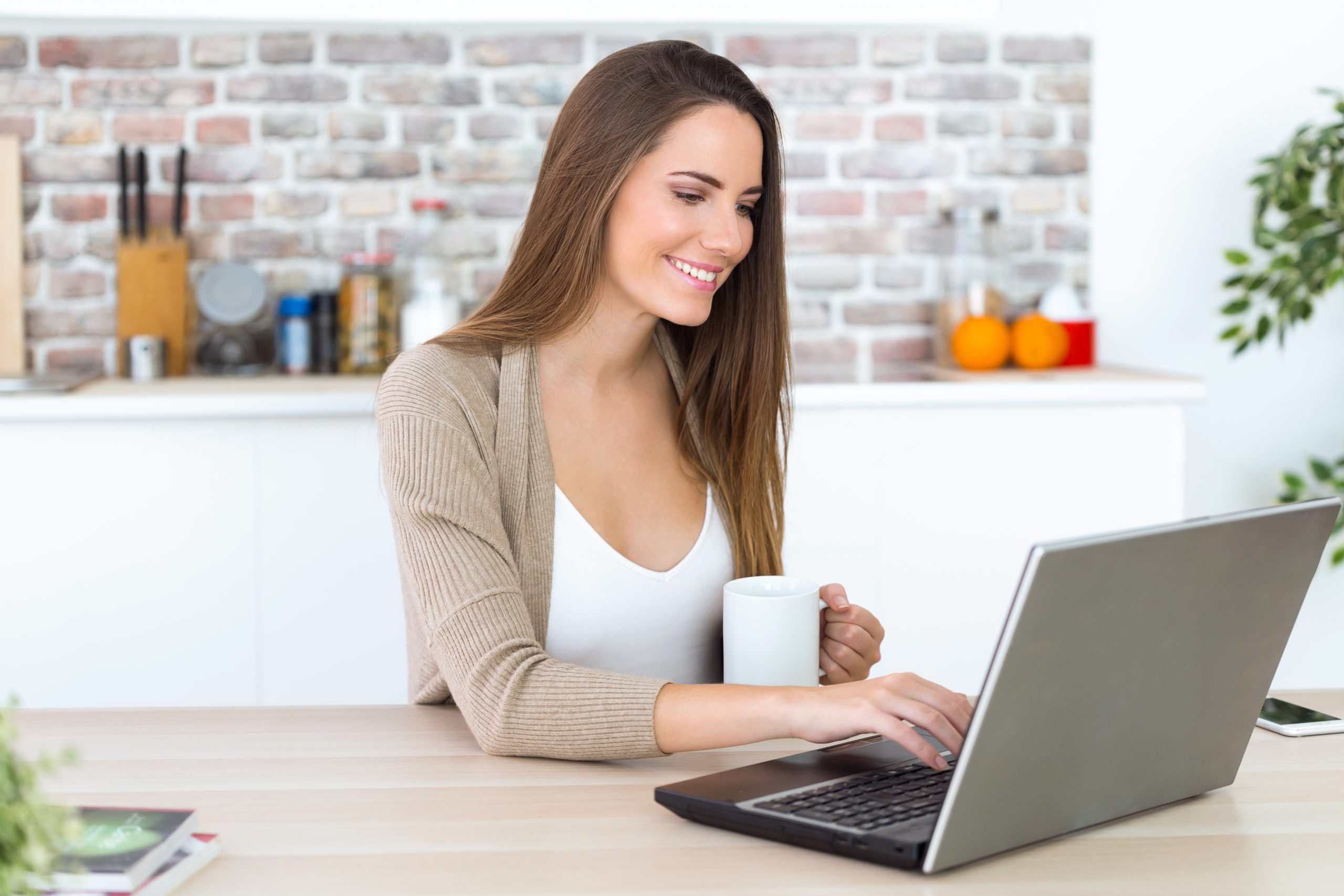 Beautiful young woman using her laptop in the kitchen. Beautiful young woman using her laptop in the kitchen.